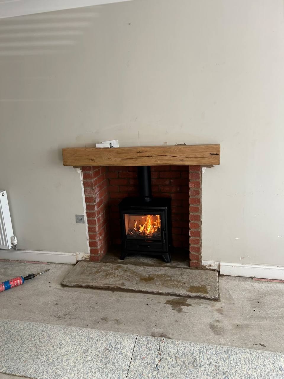 Bassington multi fuel stove in a brick chamber with side returns, rustic limestone hearth and medium oak beam, close view